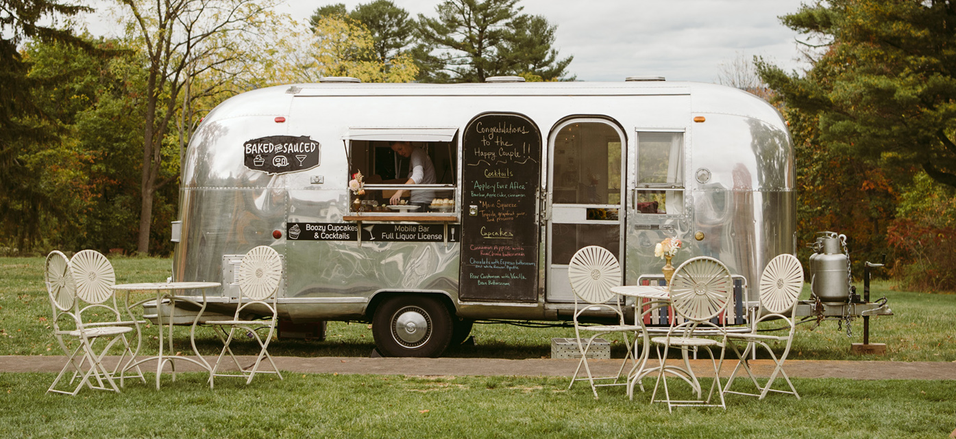 Airstream mobile bakery parked on grass with white cafe tables in front