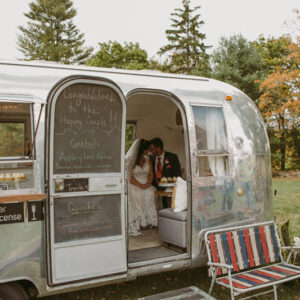 Bride and groom sitting inside Airstream mobile bakery snuggling
