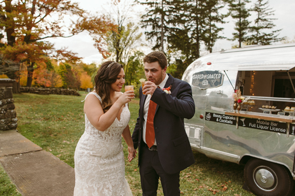 Bride and groom standing in front of airstream mobile bar and bakery drinking cocktails