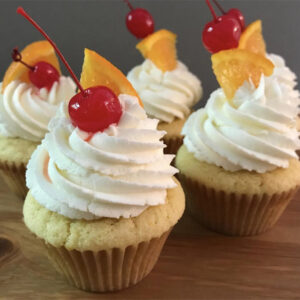 Group of five cupcakes with vanilla frosting with a cherry and orange wedge on top
