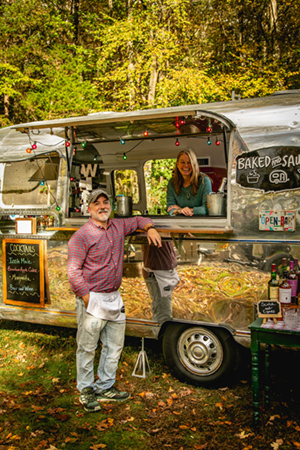 Man and woman posing with Mobile Bar & Bakery Airstream
