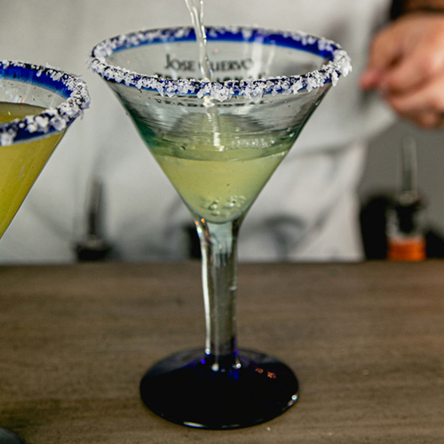 Margarita being poured into a blue glass with salt rim