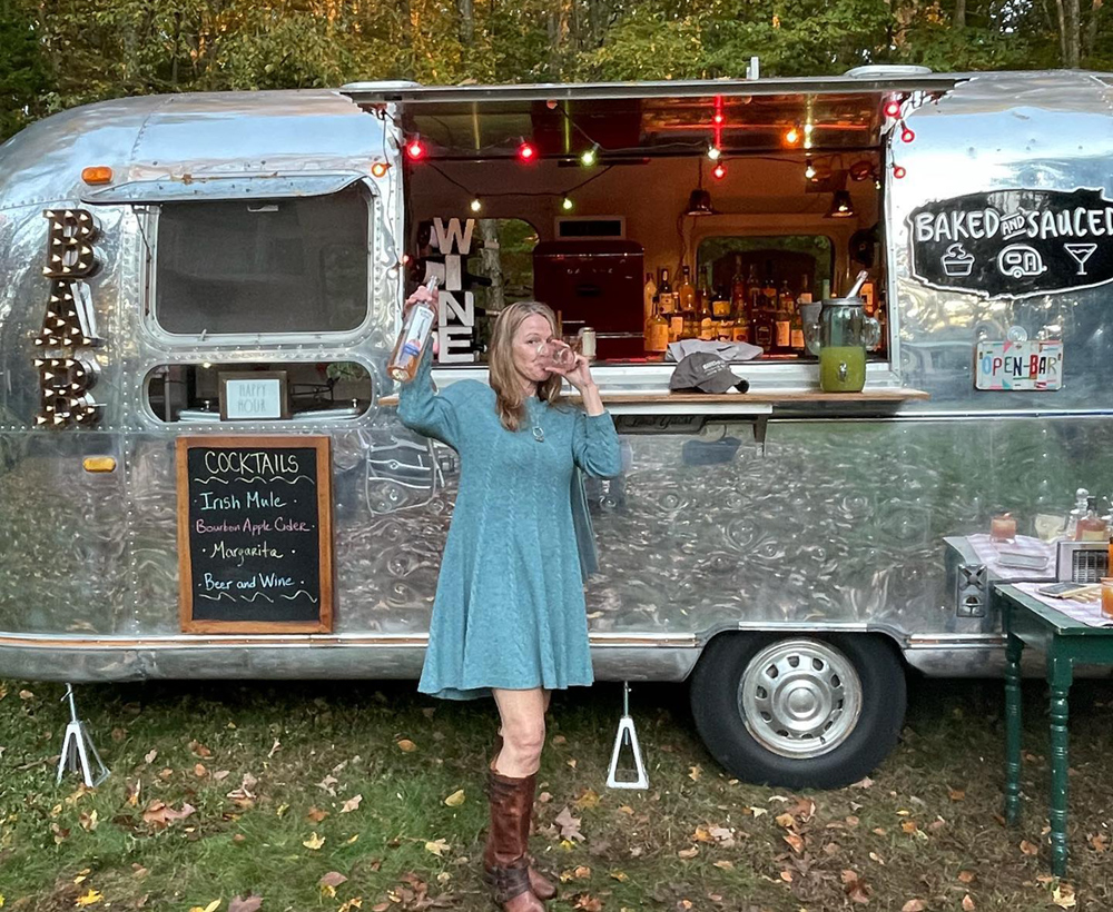 Woman standing in front of airstream mobile bar drinking glass of wine