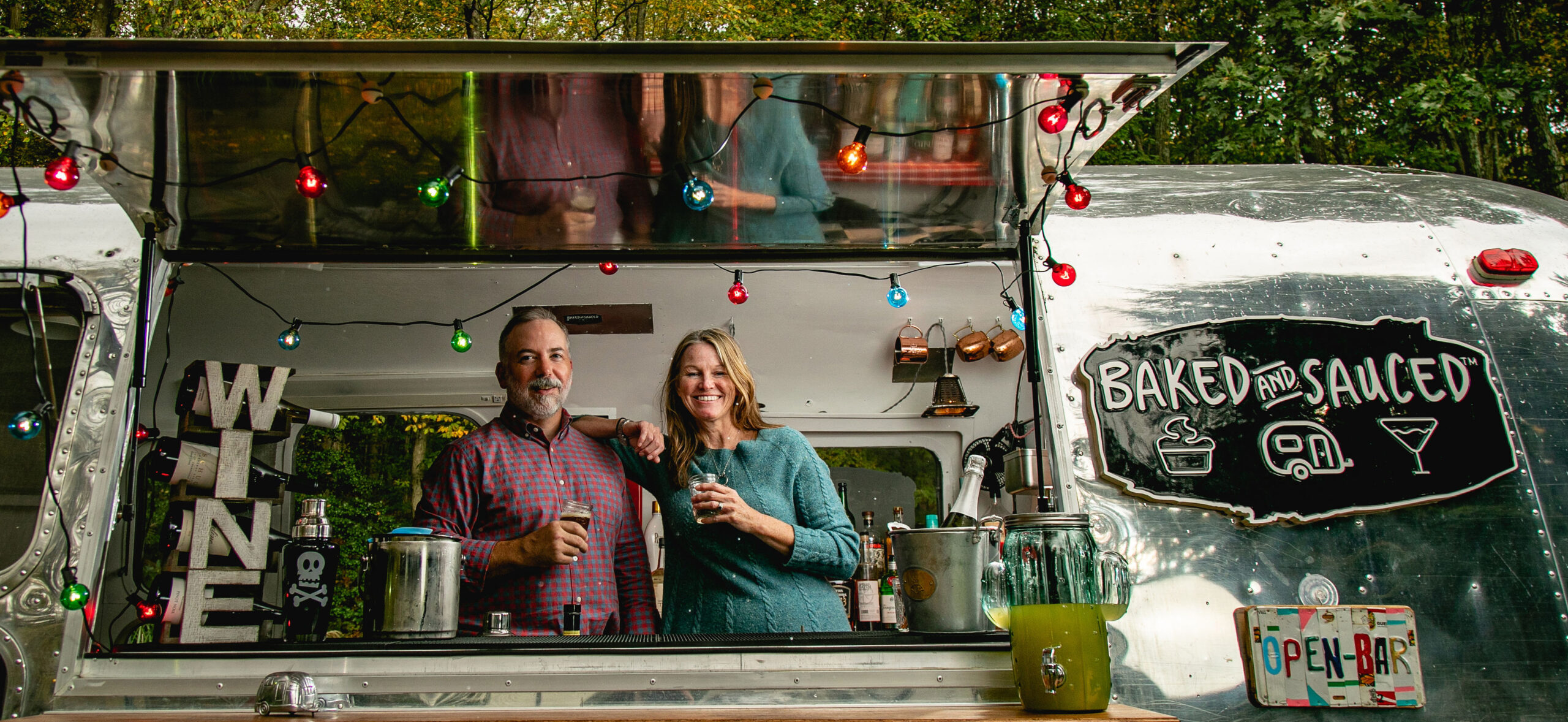 Man and woman holding drinks looking out window of airstream mobile bar